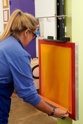A wall-mounted screen coater rack allows uniform, two-handed application of emulsions using a scoop coater.